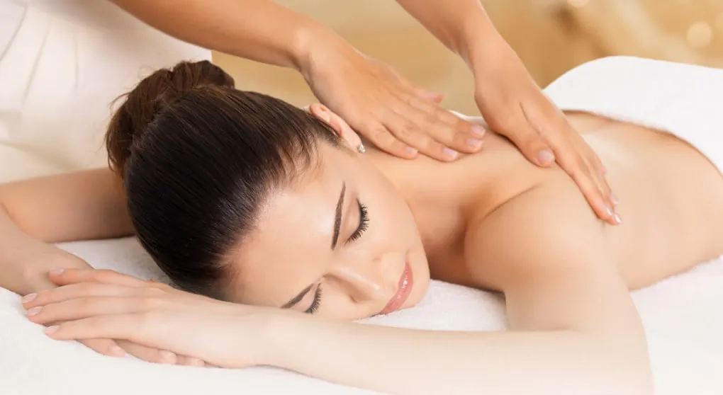 A therapist working through the upper back and shoulders during a massage session on a draped table