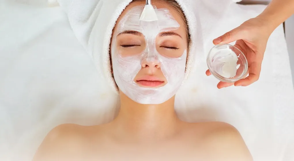 A treatment mask being smoothed onto a guest's face during a facial session