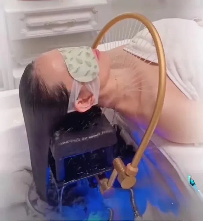 Warm water running from the gold arch rinse fixture over a guest's hair at the head spa basin in Redmond, WA