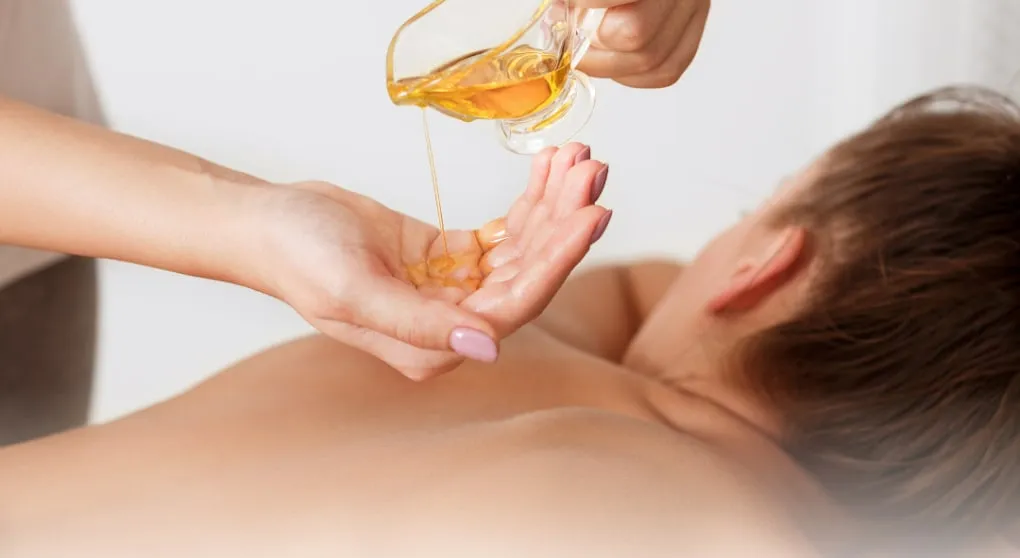 Treatment oil poured into a therapist's palm before body work in a warm, low-lit room.
